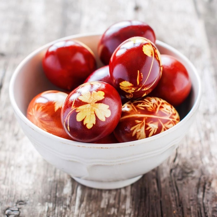 Greek red eggs with floral decorations in a white bowl on a wooden table