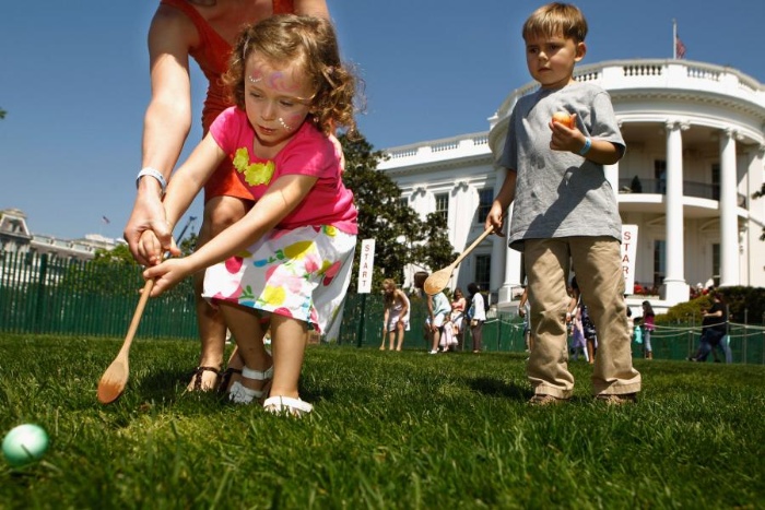 children rolling eggs with wooden spoons in front of the white house