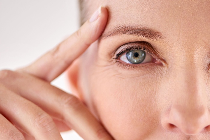 close up woman with blue eye and wrinkles holding her face