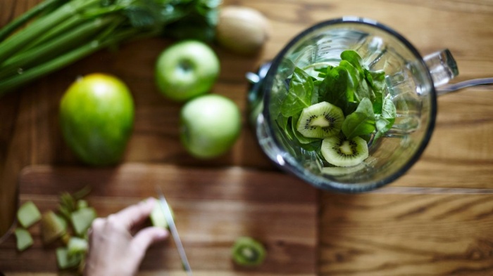 blender with kiwi and green herbs on a table with green tables and vegetables