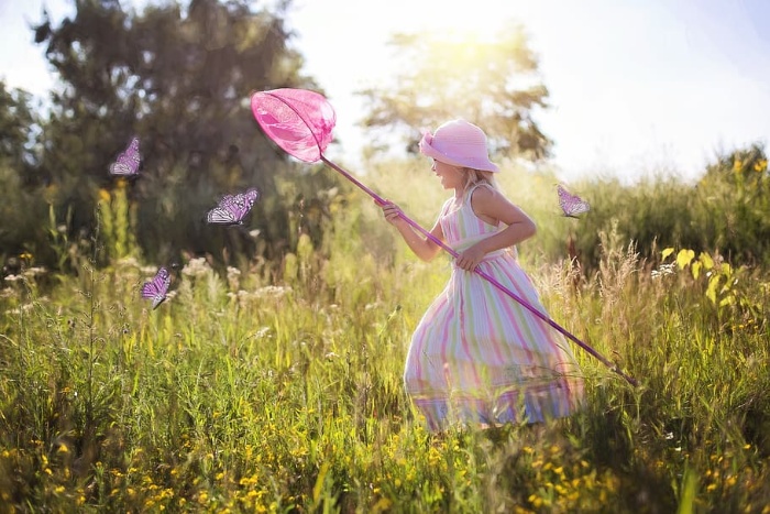 Girl in a summer dress with a pink hat in grass field chasing butterflies 