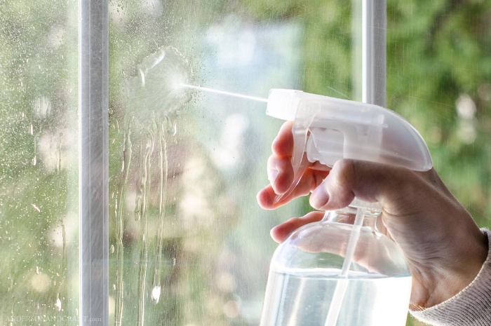 woman spraying a glass with a transparent window cleaner