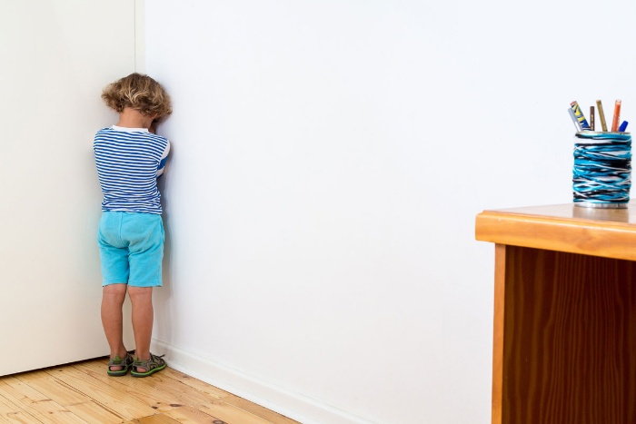 little boy dressed in blue standing in the corner 