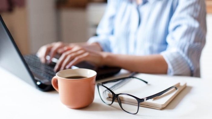 home office woman working on her laptop with a pair of glasses and a cup of coffee