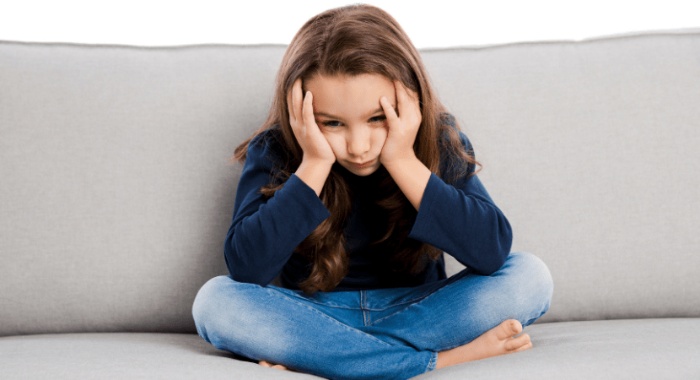 girl sitting in a sofa with her face in her hands looking sad