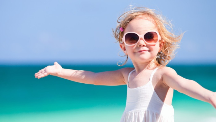 little girl in a white dress with sunglasses dancing on the beach with the sea in the background