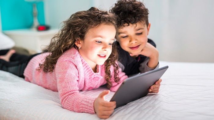 kids screen time little girl and boy laying in bed looking at a tablet