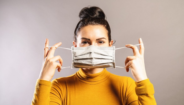 woman with black hair and yellow turtleneck blouse putting mask down