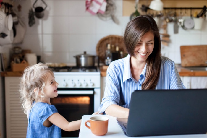 working from home with kids woman sitting in front of a laptop smiling and working with a little grl by her side