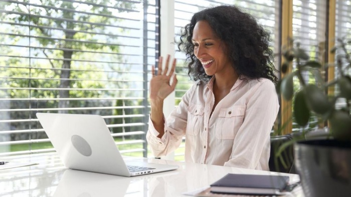 working from the house women waving at a white laptop in front of a window