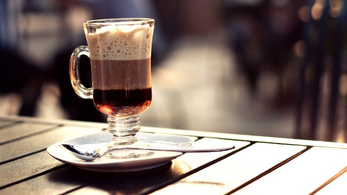 Irish coffee on a wooden table outside in the sun with a plate and spoon