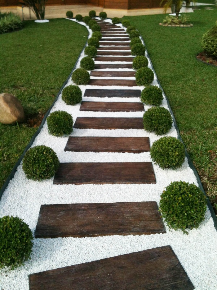 beautiful walkway with wooden steps and white stones and green decorative shrubs