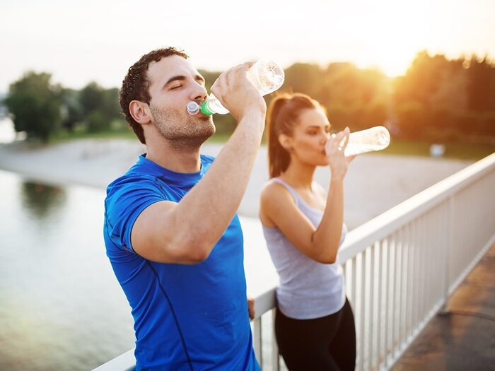 hydration after spot a man and a women drinking water from bottles on a bridge over a river