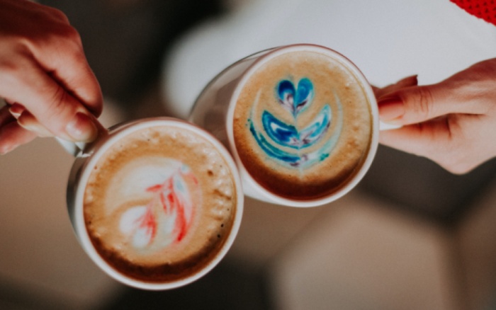 two people cheering with two mugs of coffee with cream and colorful applications on it