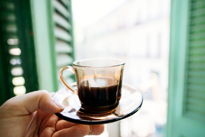 hand holding a glass with cuban coffee in front of a window with green shutters