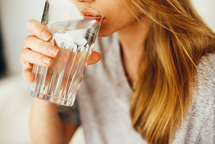 driniking water for optimal hydration blond girl with a grey shirt drinking water from a big glass