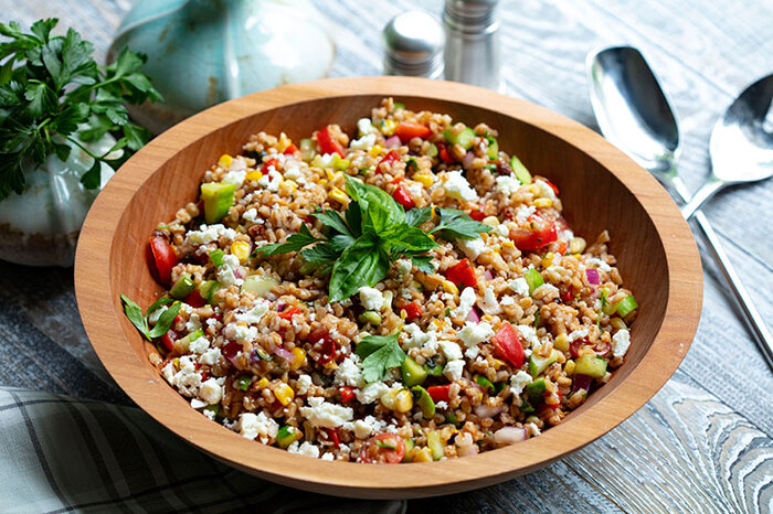 farro salad in a large wooden bowl with two spoons on a grey table