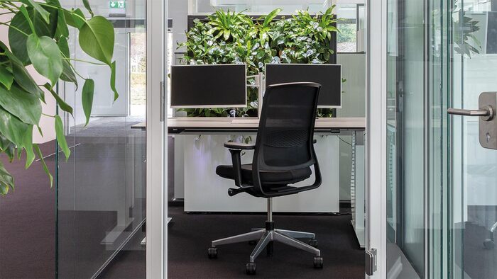 home office with living plants biophilic design with a chair and two monitors and glass