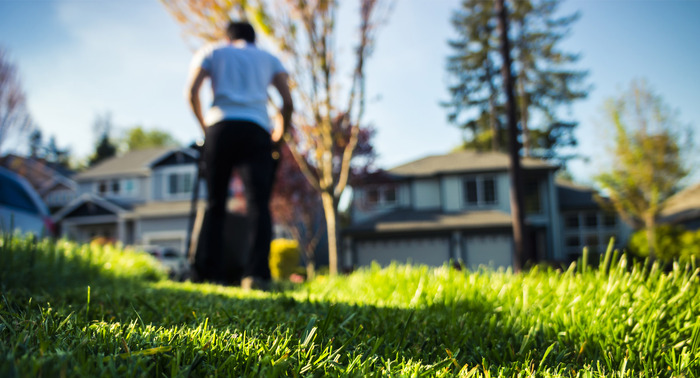 man mowing a lawn with green grass houses in the background