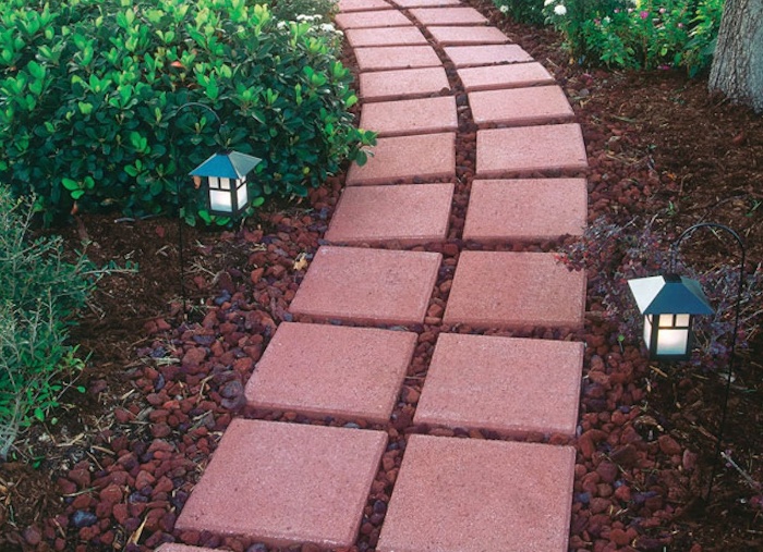 red tile pathway in a garden surrounded by red stones and lamps