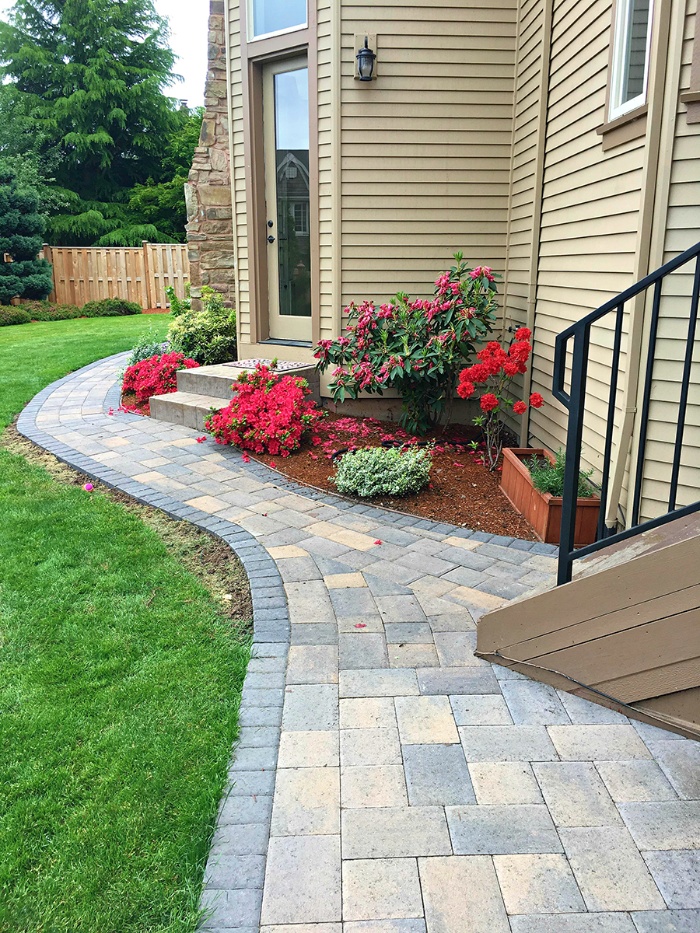 paver pathway in grey and beige around a beige home with flowers in front