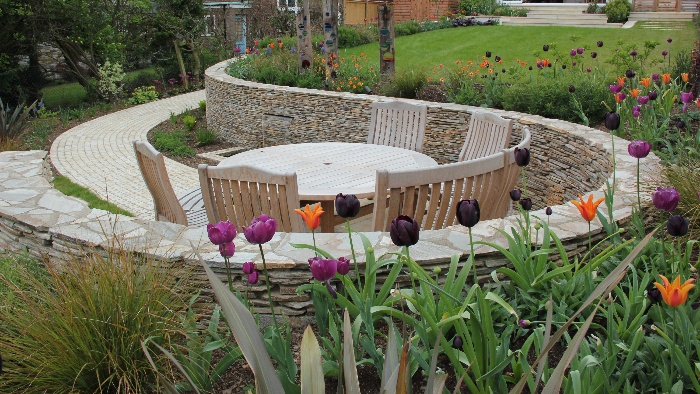 sloped backyard with a wooden table and chairs surrounded by tulips