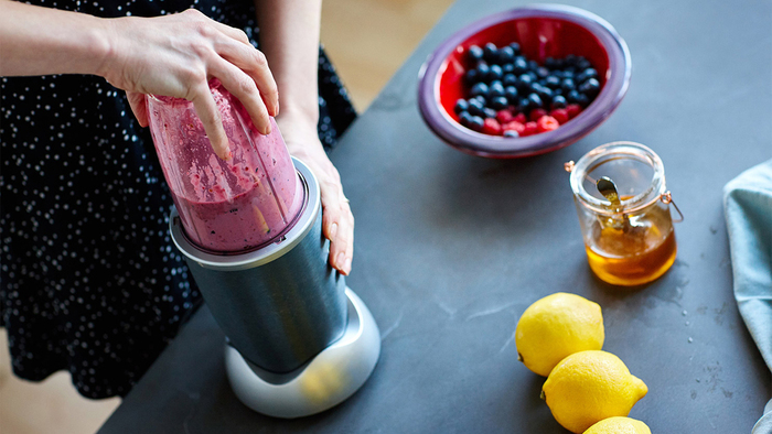 woman preparing a smoothie with berries honey and lemons in a blender