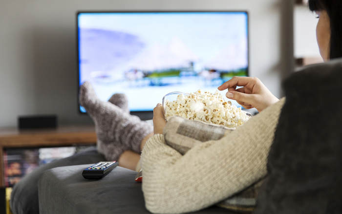 woman in sweater and socks sitting in front of the tv with a bowl of popcorn 