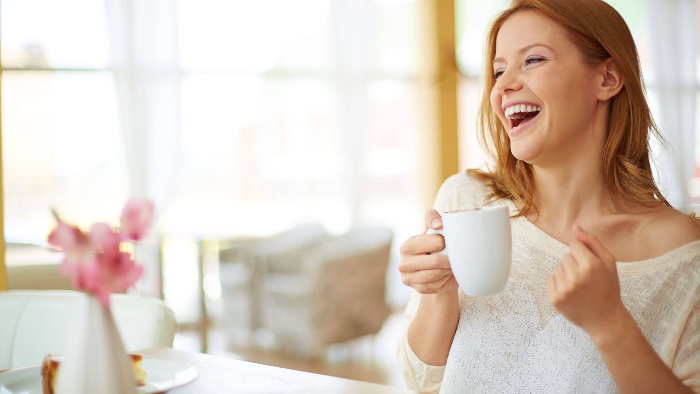 woman drinking coffee in a white mug and laughing