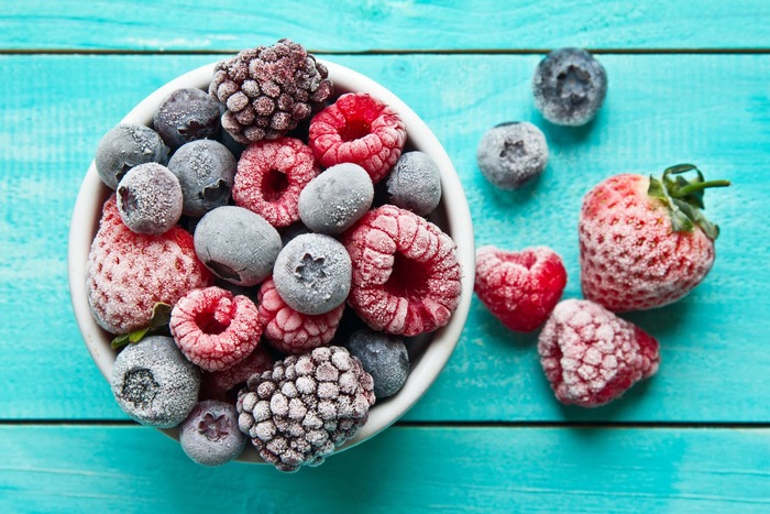 frozen berries in a white cup on a light blue wooden table