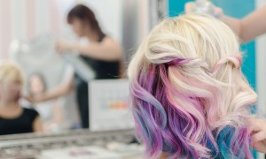 Hairdresser spraying hair spray on the female finished haircut. She love her new look and watching herself in the mirror. Love unicorn and rainbow hair.