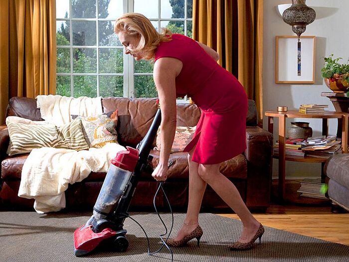 Woman in a red dress and high heels vacuuming with a red machine in a living room