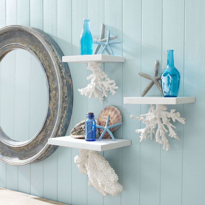 sea themed bathroom decor with a grey mirror and little white shelves with blue bottles and shells