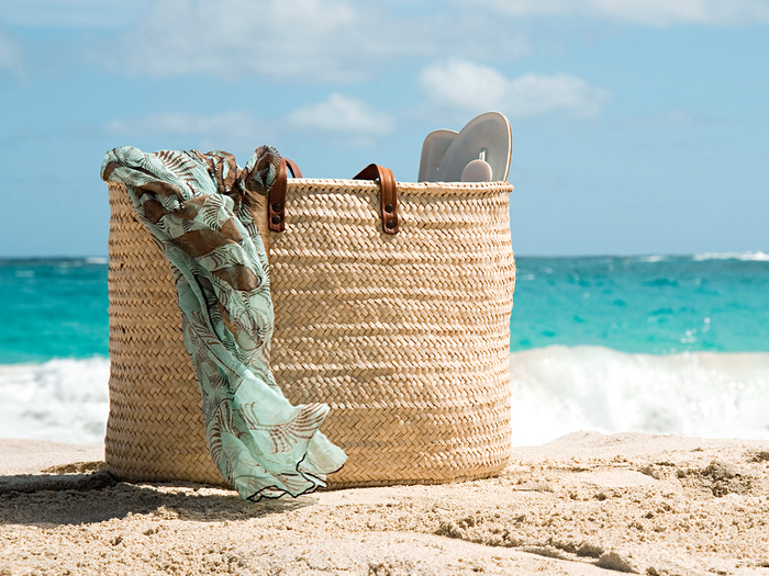 beach bag with a blue scarf coming out of it on the sand with the sea in the background