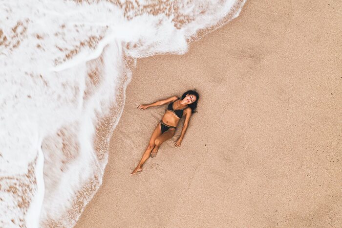 beach girl woman in a black swimsuit lying on the beach with waves coming at her