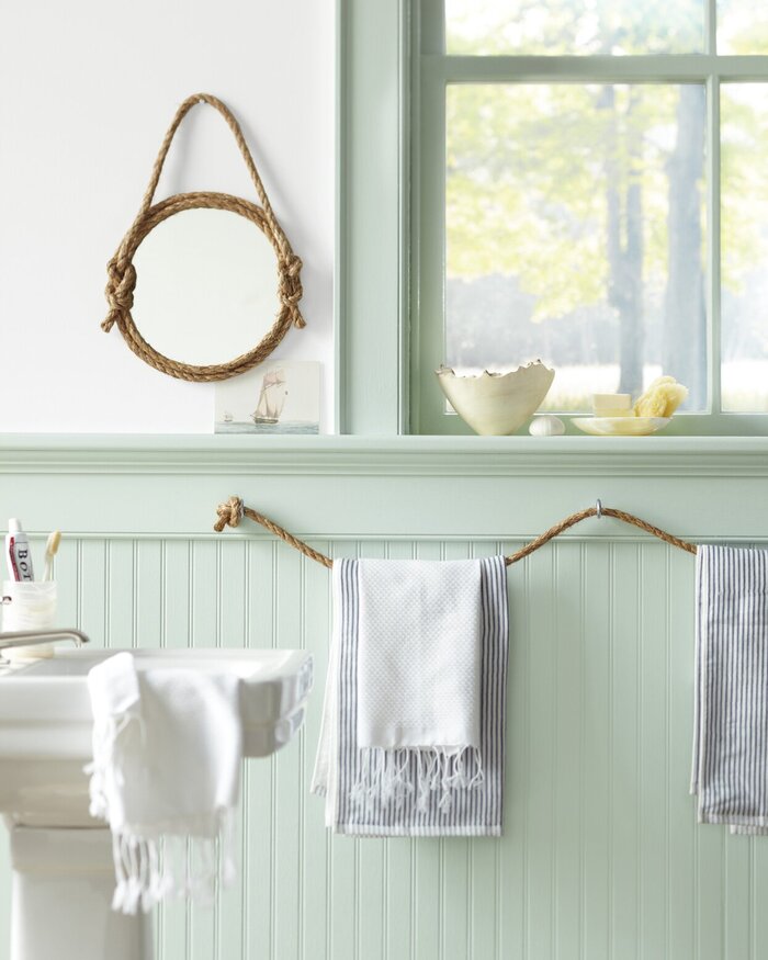beach themed decor minty green bathroom with a mirror on the wall next to a window white towels and rope accents