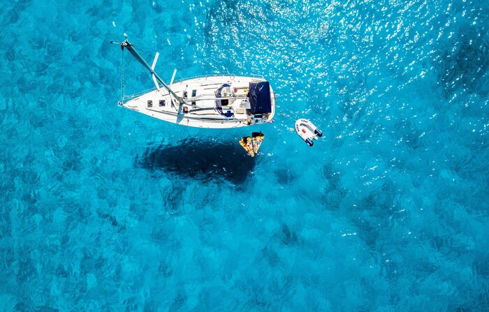 a white boat in the middle on a light blue sea with people lounging in the water