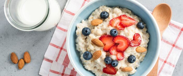 cereal and oatmeal breakfast with fruits and nuts on a white and red towel with a wooden spoon