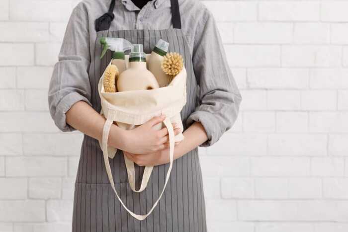 cleaning supplies person with a grey apron and a grey shirt holding a white bag with cleaning supplies