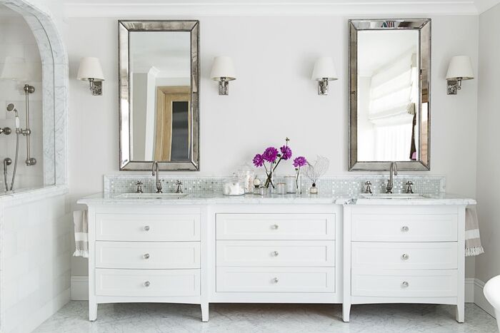 modern white bathroom with two silver framed mirrors and white furniture