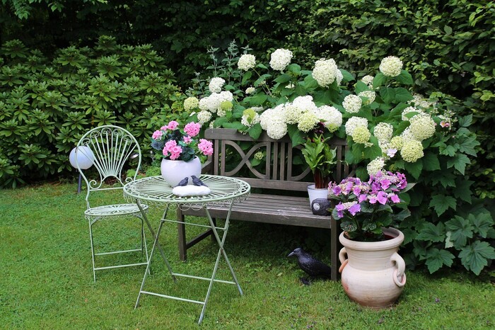 cute garden spot with a table chair and a bench with flowers all around