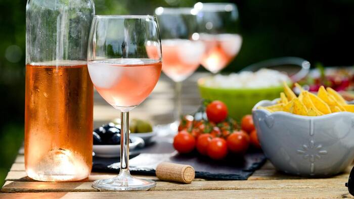 delicious rose wine into glasses surrounded by various snacks