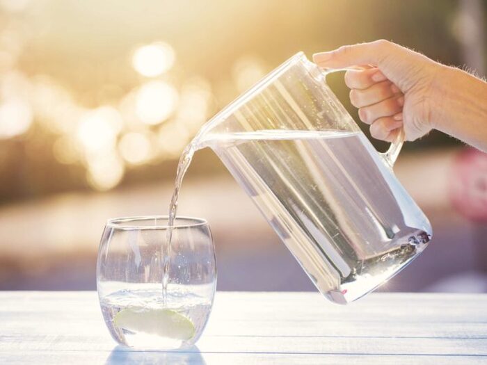 drinking water large jug of water and a glass hand pouring water in the glass on a table