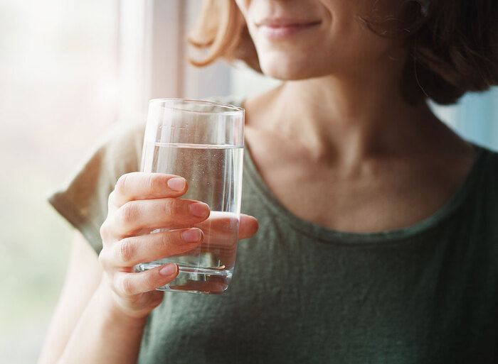 woman in a green shirt with short hair holding a glass of water looking through the window