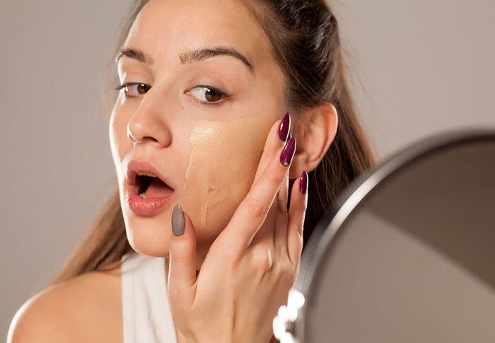 woman applying foundation on her face looking in the mirror