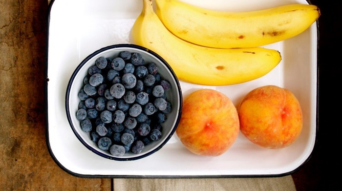 fruit serving blueberries peaches and bananas on a white tray on a wooden table