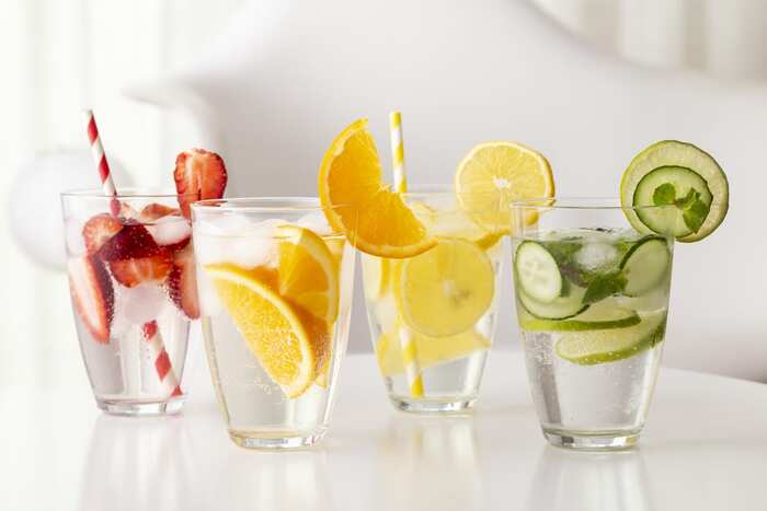 glasses with infused fruit water with cucumber strawberries orange lemon and colorful straws