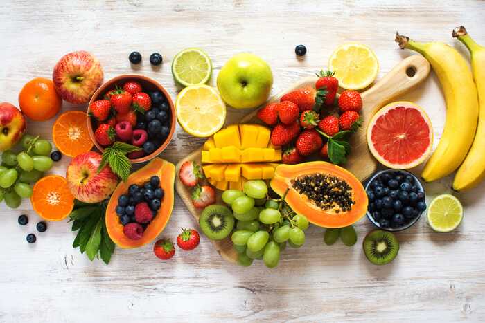 different fruits arranged on a white wooden table tropical fruits grapes bananas papaya limes and other fruits