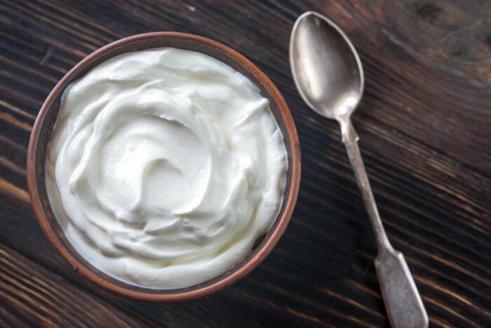 energy foods greek yoghurt in a brown bowl on a wooden table with a spoon next to it