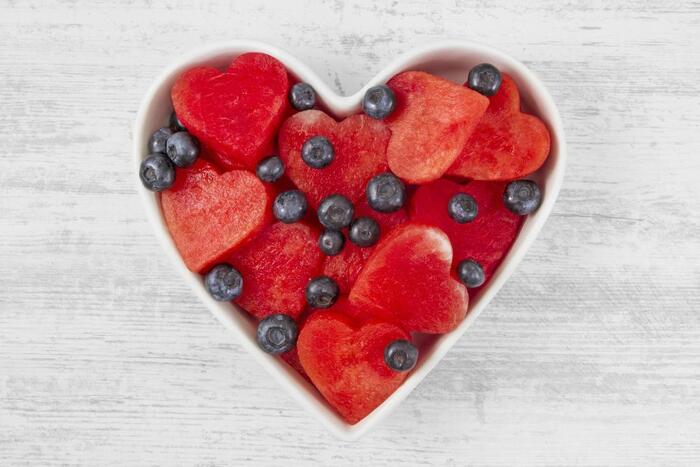 heart shaped bowl on a white table with hearts cut of watermelon and blueberries